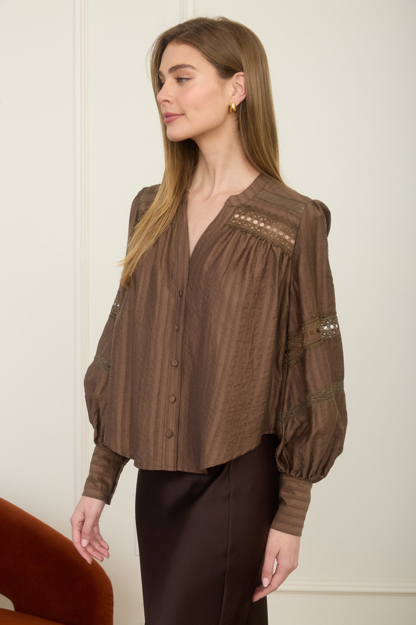 A woman wearing a romantic, flowy espresso brown long-sleeve peasant blouse with detailed ladder-lace inserts across the chest and sleeves.