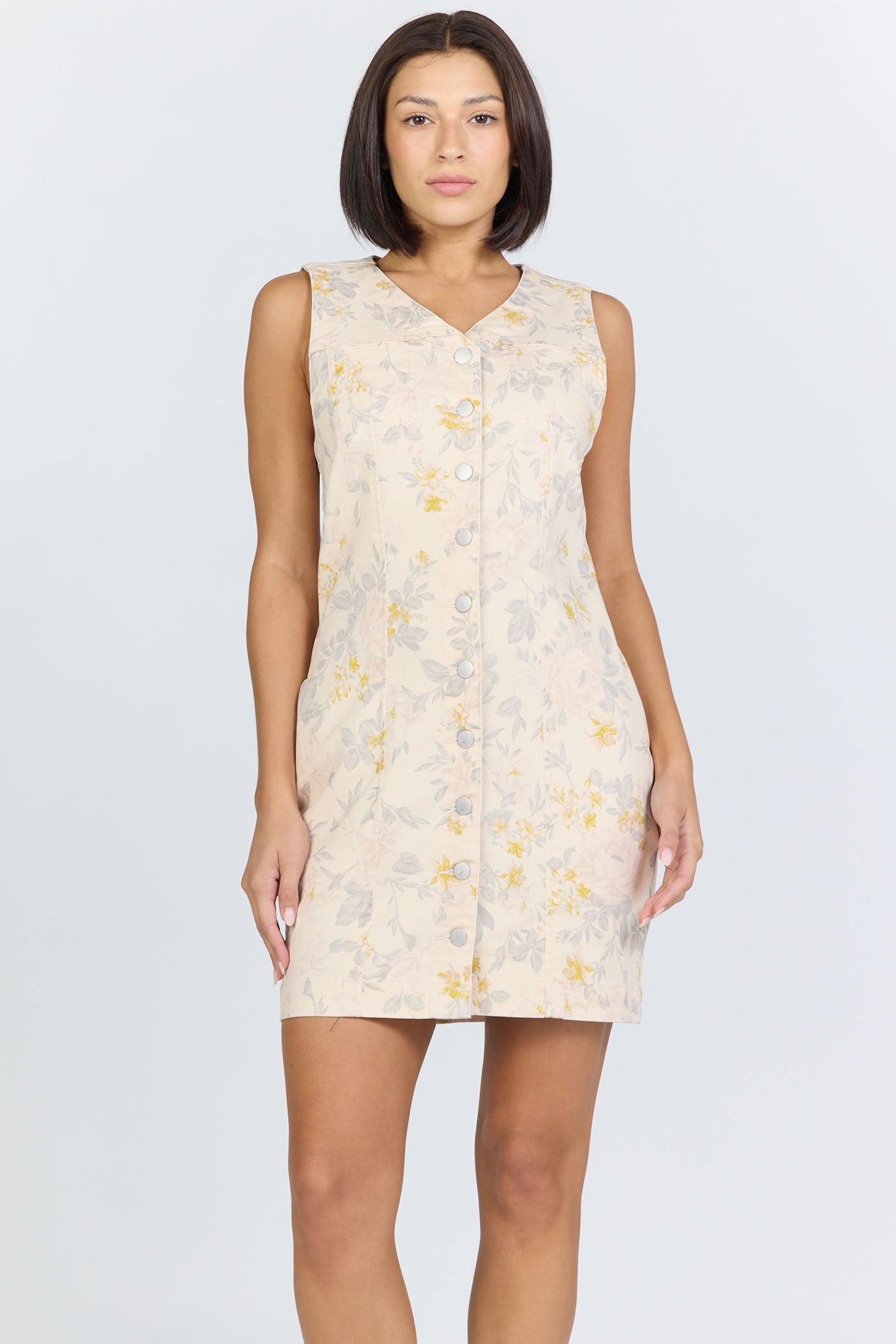 Front view of a model with short dark hair wearing a cream floral button-front sleeveless dress.