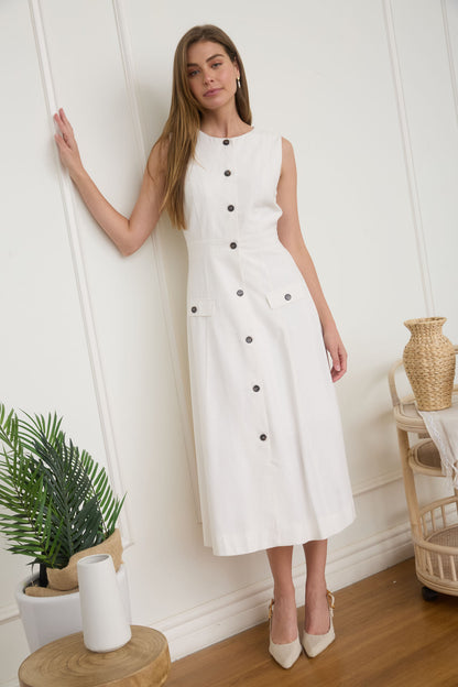 A woman wearing a sleeveless, button-front white midi dress with faux hip pockets and low heels.
