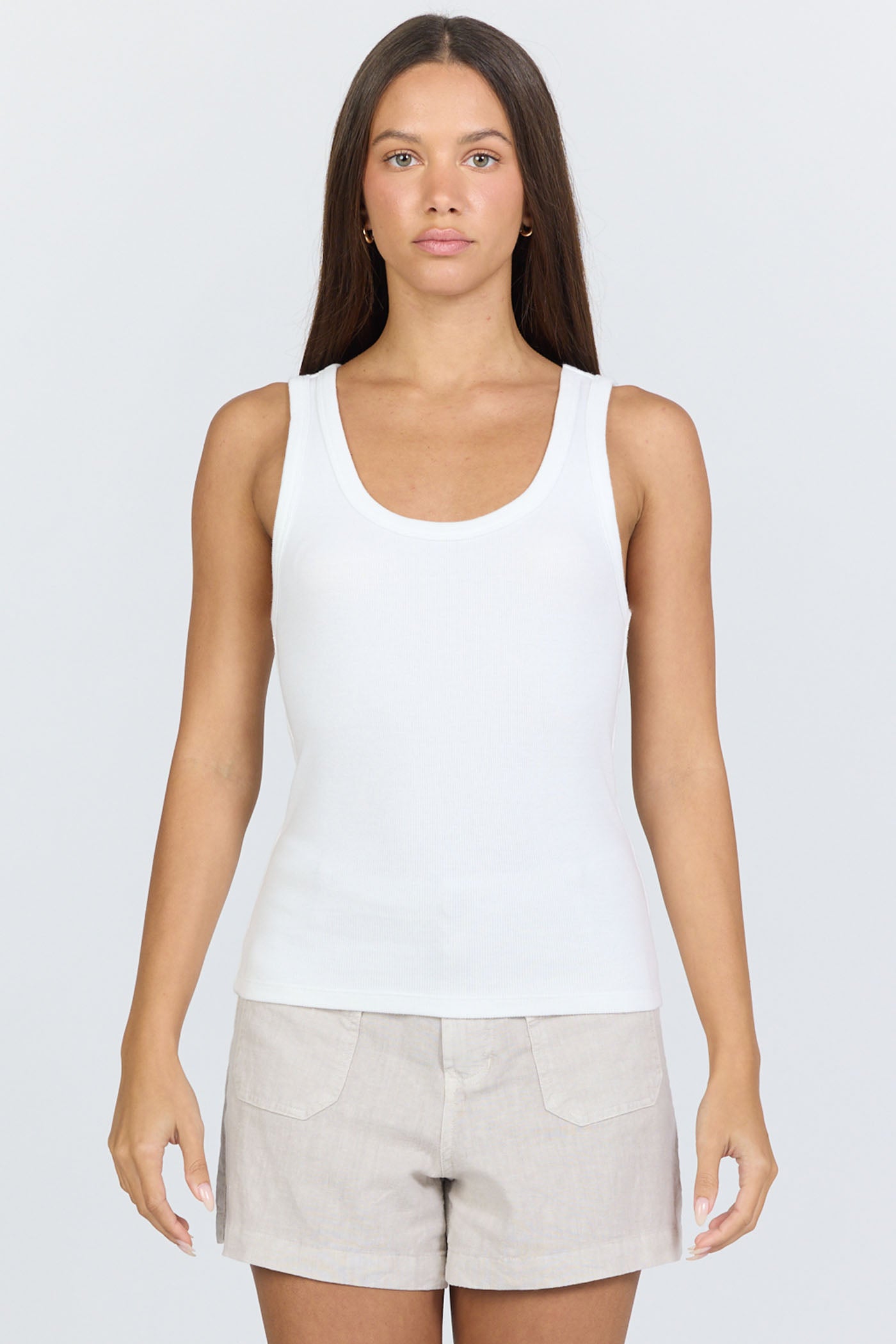 A woman wearing a fitted white scoop-neck ribbed racerback tank top with beige linen shorts.