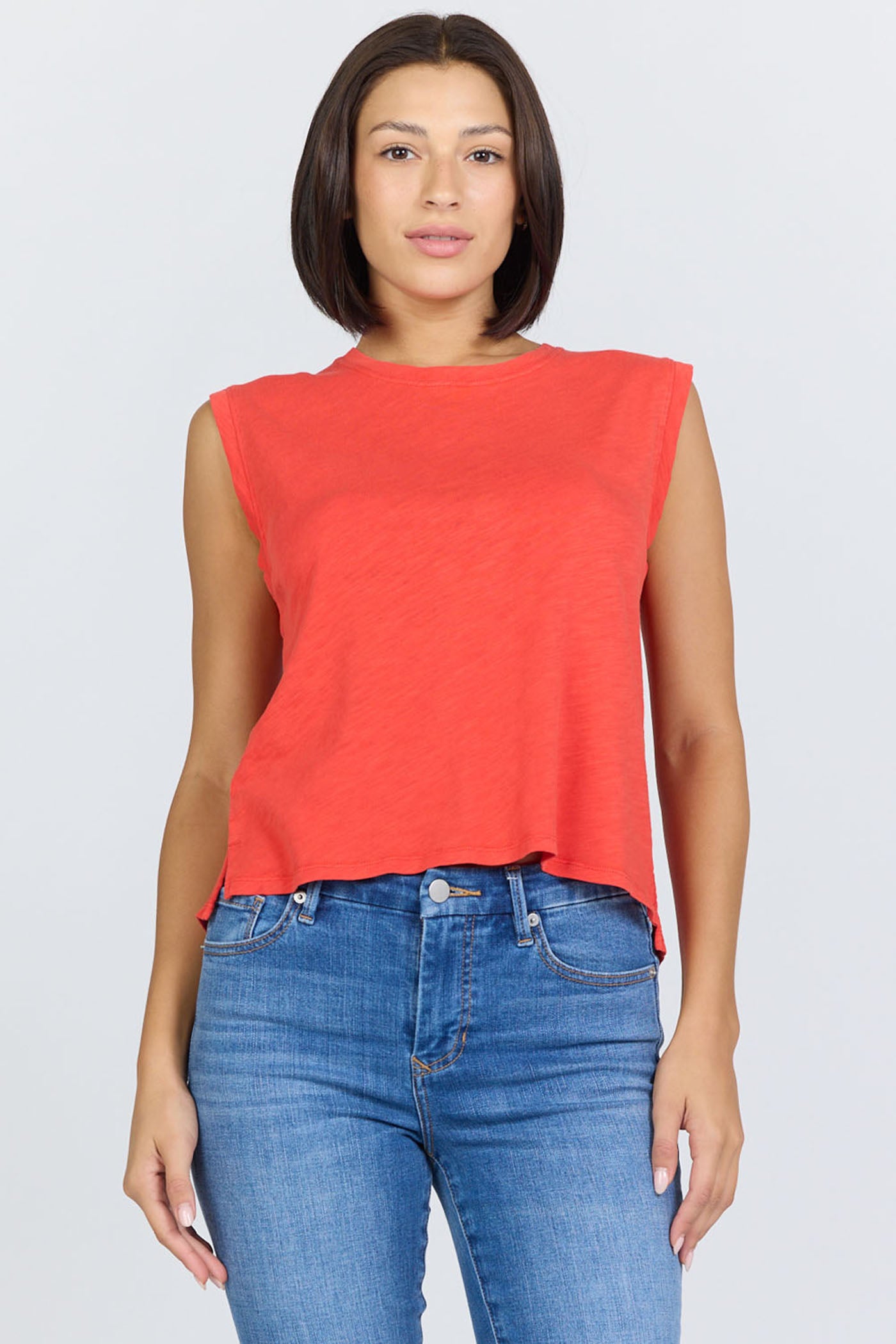Woman wearing a poppy red sleeveless crew neck muscle tank made from textured slub cotton, paired with blue jeans.